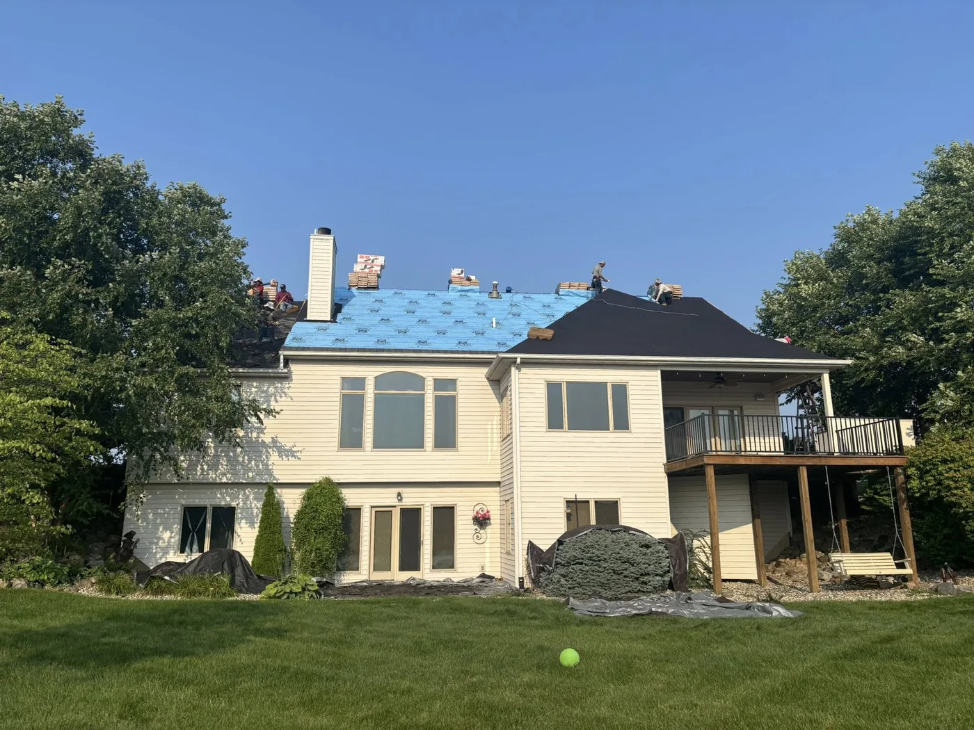 Roofing crew mid-installation laying new shingles over blue underlayment on a residential home